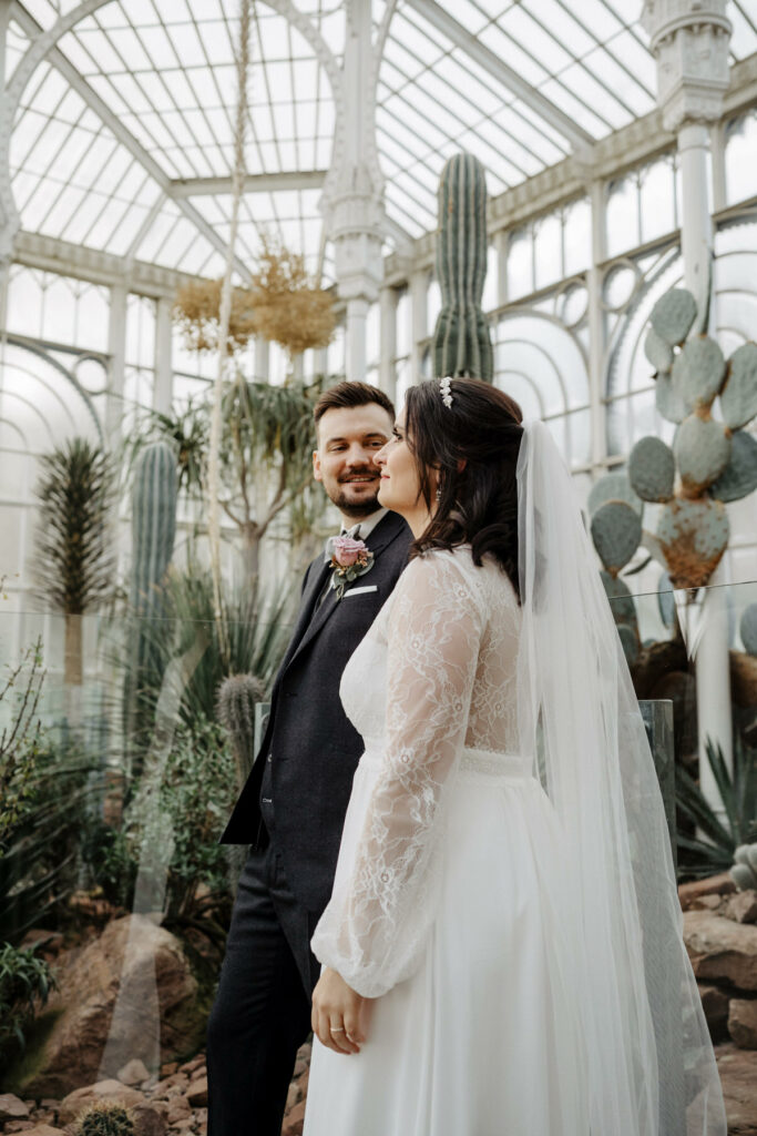 Braut und Bräutigam stehen im Gewächshaus vor Kakteen und Palmen